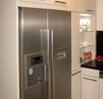 Integration des Amerikanischen Kühlschrankes durch Wangen und Klappschränke sowie deckenhohe Verkleidung aus Küchenmaterial
